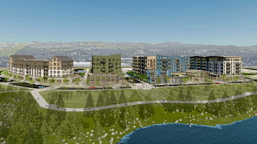 A modern building complex is situated by a body of water with a mountainous background.