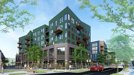 A modern building with a green facade and balconies is surrounded by trees and a street with cars.
