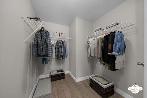 A white closet with clothes hanging on racks and a wooden bench underneath.