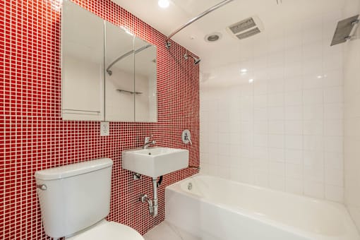 A red tiled bathroom with a white toilet, sink, and bathtub.