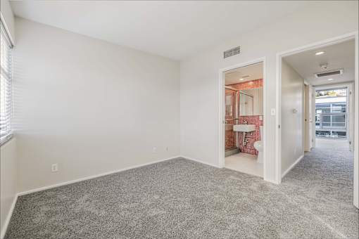 A room with a carpeted floor and a bathroom visible through an open door.