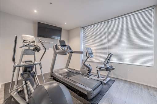 A home gym with a treadmill, elliptical trainer, and a television.