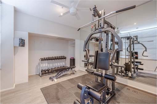 A home gym with a variety of equipment including a weight bench, dumbbells, and a cable machine.
