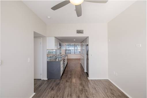 A spacious room with a ceiling fan and a kitchen area in the background.