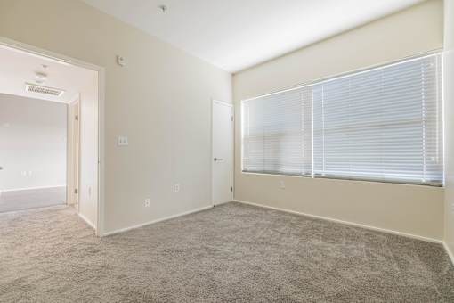 A room with a carpeted floor and a window with blinds.