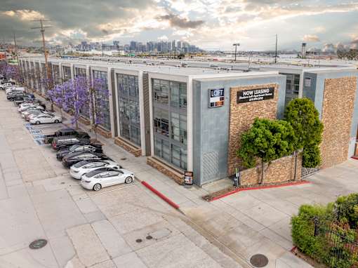 A parking lot with a white car parked in front of a building that has a sign that says "Now Leasing".