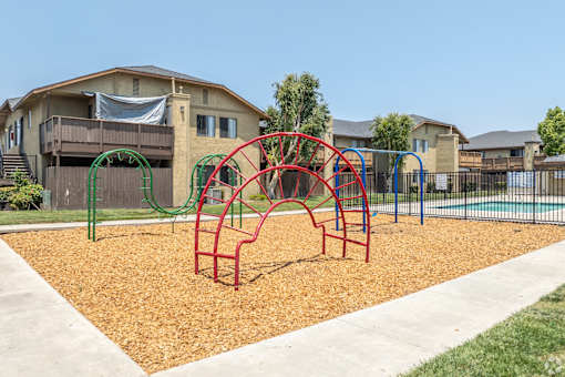 A playground with a red and green swing set in front of apartment buildings.