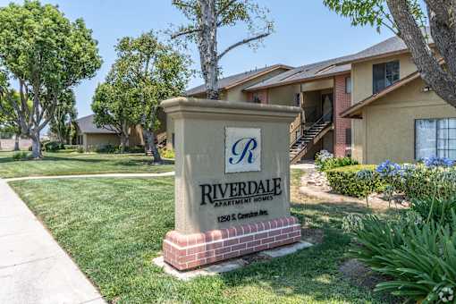 A sign for Riverdale Apartment Homes stands in front of a building.