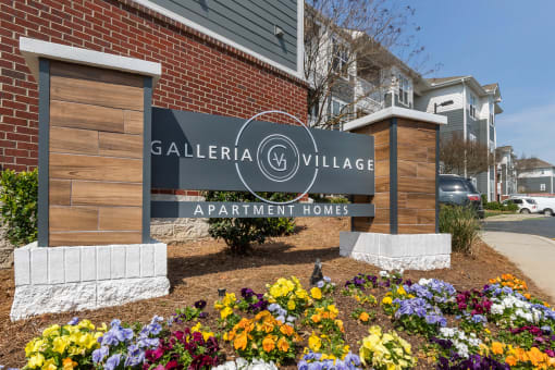 a sign that says galeria village apartment homes with flowers in front of it