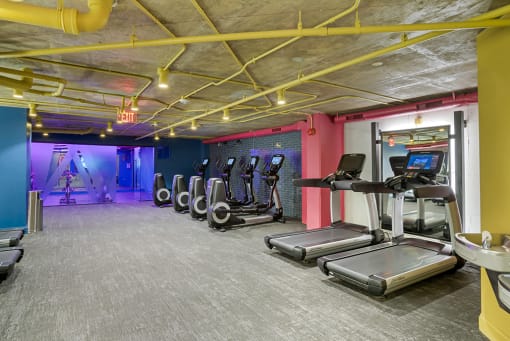 a gym with cardio equipment and a colorful wall in a building