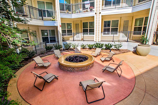 A patio with chairs and a fire pit in the middle of a courtyard.