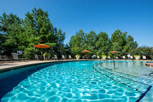 A large swimming pool with a blue tinted water and a sun umbrella.