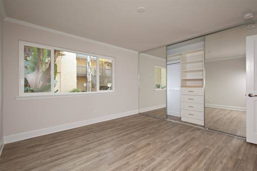 A room with wooden flooring and a large window with a view of a building outside.