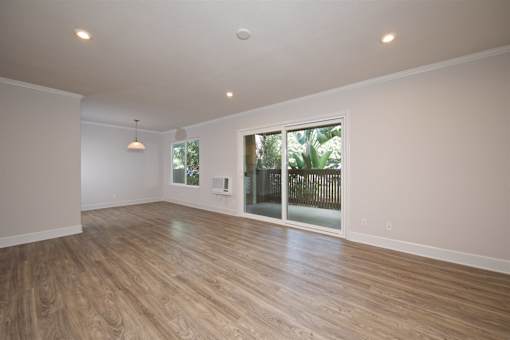 A room with wooden flooring and a sliding glass door leading to a backyard.