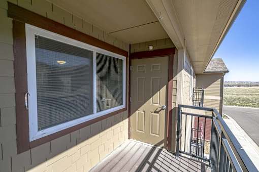 A balcony with a brown door and a window with blinds.