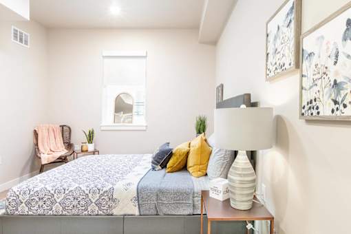 A bedroom with a bed, a chair, a lamp, and a painting on the wall.