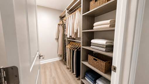 A white closet with clothes and towels.