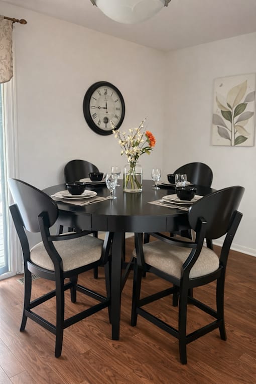 A black dining table with four chairs and a vase of flowers on top.