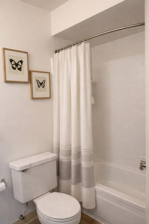 A white toilet sits next to a white shower curtain in a bathroom.