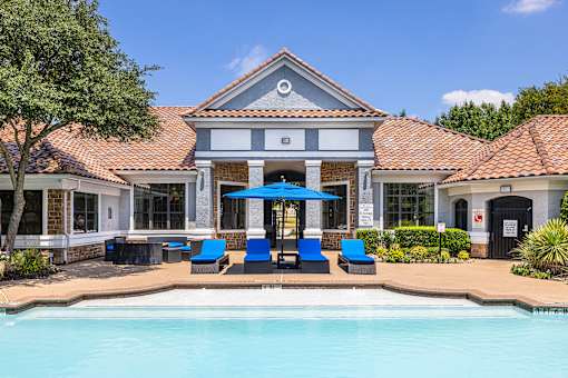 A pool area with a building and blue loungers.