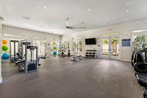 A spacious gym with a variety of equipment and a ceiling fan.
