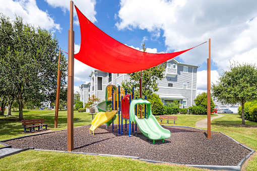 A playground with a yellow slide and a red shade sail.