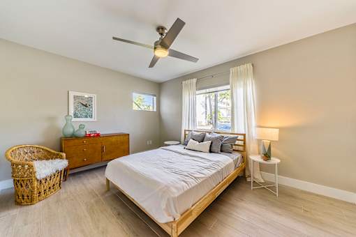 A bedroom with a bed, a chair, a nightstand, and a ceiling fan.