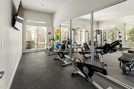 A gym with a mirrored wall and various exercise equipment.