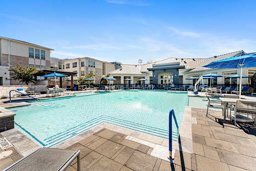 A large swimming pool surrounded by a tiled patio and lounge chairs.