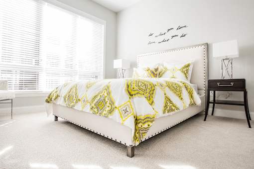 A bed with a yellow and white comforter sits in a bright bedroom.
