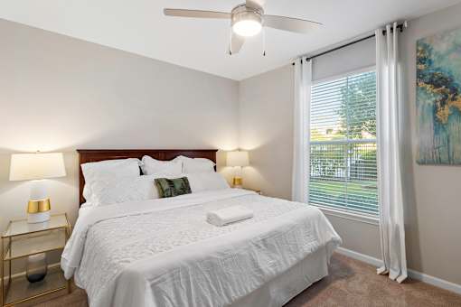 A bedroom with a large bed, a ceiling fan, and a window with white curtains.