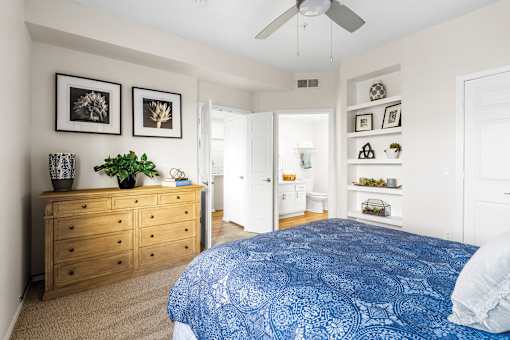 A bedroom with a blue bedspread and a wooden dresser.