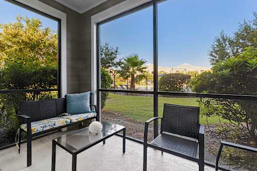 A balcony with a sofa, table, and chairs overlooking a garden.