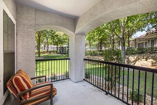 A patio with a striped chair and a view of a fenced yard.