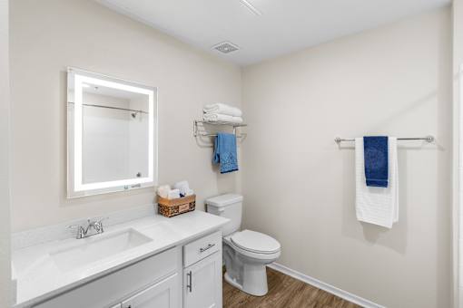A white bathroom with a toilet, sink, mirror, and towel rack.