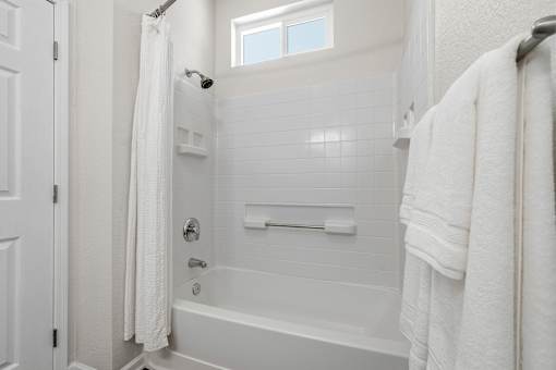 A white bathroom with a tub, towel, and shower curtain.