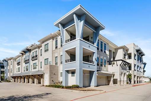 A large, modern apartment complex with multiple balconies and a clear blue sky above.