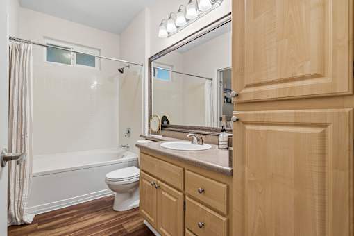 A bathroom with a wooden cabinet, a white toilet, and a white bathtub.