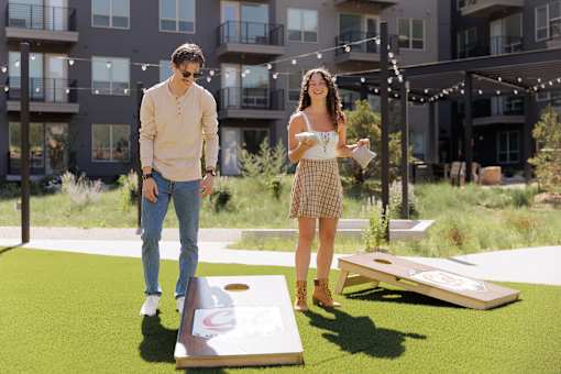 A man and a woman are playing a game of cornhole in a grassy area.