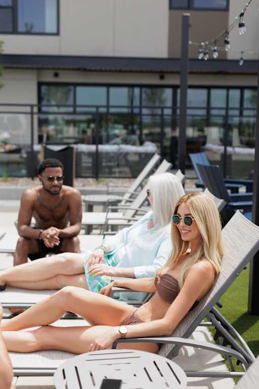 Three people sunbathing on lounge chairs by a pool.