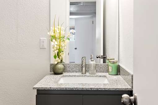 A bathroom sink with a green jar and a vase with white flowers.