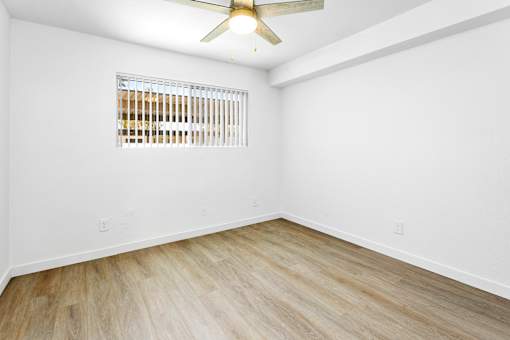 A room with a ceiling fan and a window with blinds.