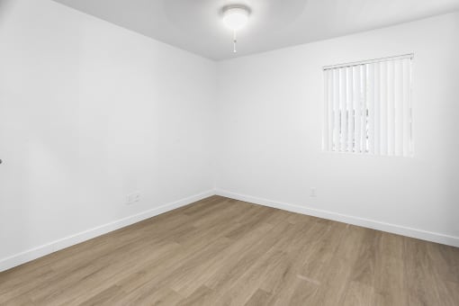 an empty room with white walls and wooden floors and a window