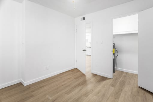 a bedroom with white walls and wood flooring and a door to a bathroom