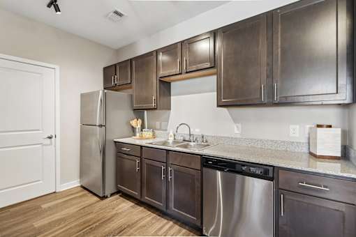 A kitchen with a stainless steel refrigerator and dark brown cabinets.