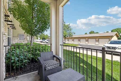 A chair and ottoman are on a porch with a tree and a building in the background.