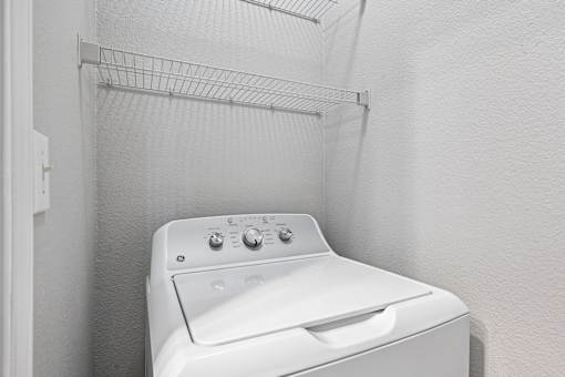 A white dryer is sitting in a small, white-walled laundry room.
