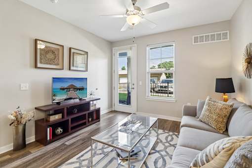 A living room with a grey couch, a glass coffee table, and a painting of a beach house on the wall.