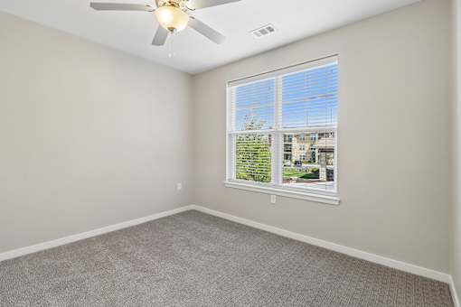A room with a ceiling fan and a window overlooking a building.