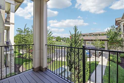 A balcony with a black railing and a view of a street and trees.
